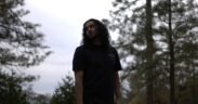 Rapper Bandzo3rd with long hair wearing black in a forest