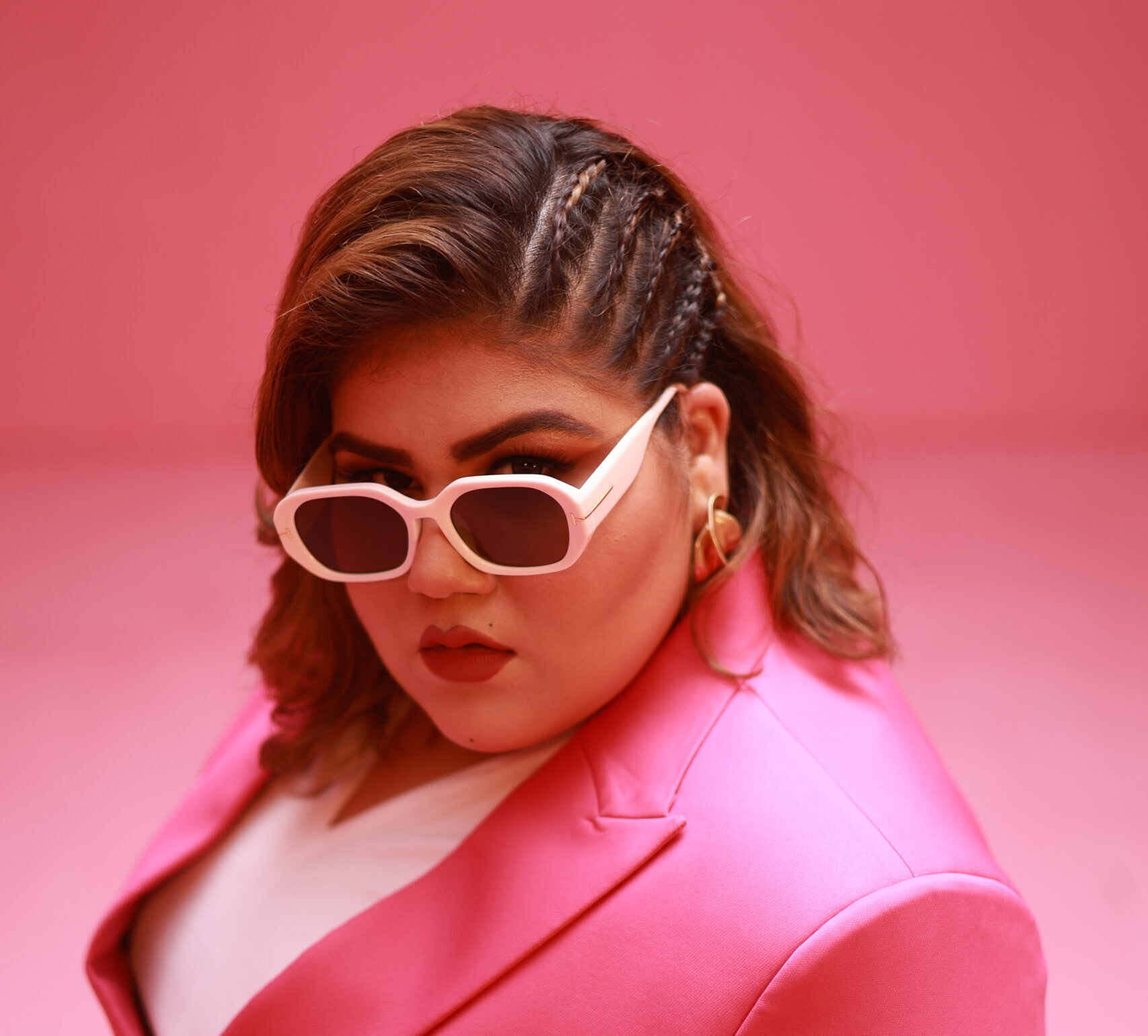 Simiran Kaur Dhadli wearing white framed glasses and a pink suit with braids in her hair