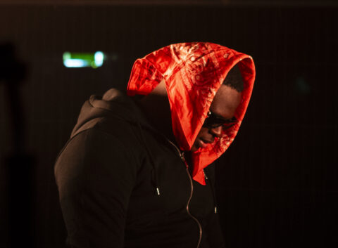 Nigerian rapper Yung Sammy wearing a red bandana and black jacket in the video for 'The Intro' for DESI TRILL