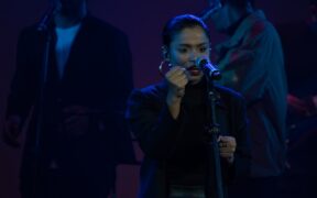 Arunaja wearing black and singing with hand raised