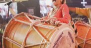 Purva Mantri smiling in red sari, beating dhol drum