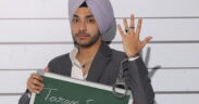 Actor Taran Singh in a suit, handcuffs on one hand, holding a chalkboard