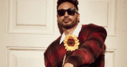 Arjun Kanungo in a plaid red shirt wearing sunglasses and holding a sunflower