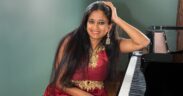 Charu Suri seated in a red dress with hand on piano