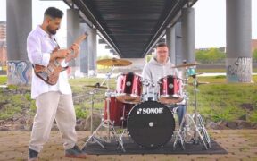 Fahd Wani playing guitar and Sam Schwarzer playing drums in a open area under a bridge