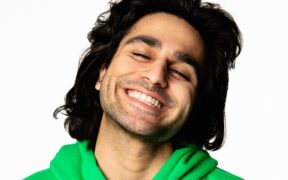 Indo-American rapper KOAD smiling with eyes closed, wearing green hoodie