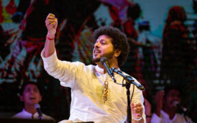 Mahesh Kale in white kurta singing into mic, hand raised