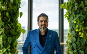 Ricky Kej in a blue coat smiling with greenery in background