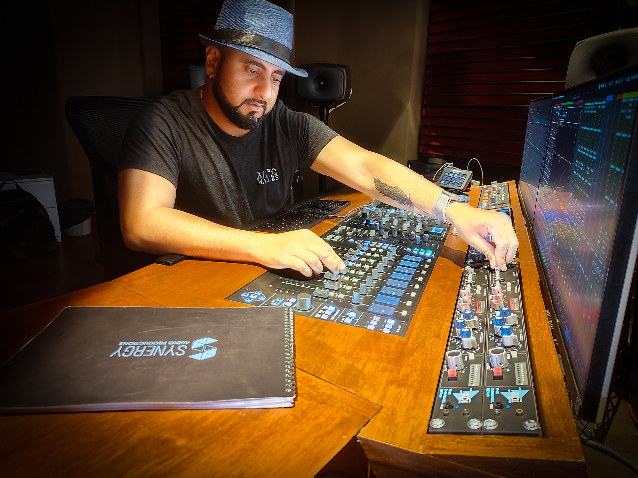 Rohan Solomon wearing a hat and seated at mixing and marketing studio sound board