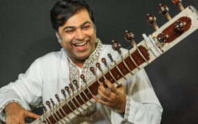 Purbayan Chatterjee wearing white, smiling and playing sitar