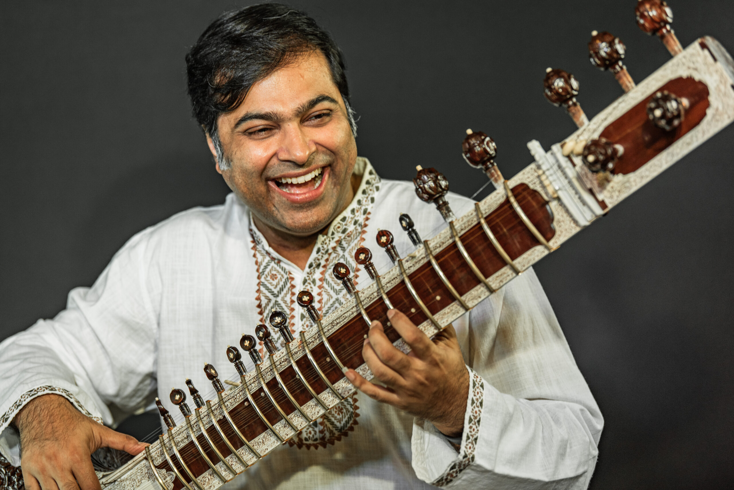 Purbayan Chatterjee wearing white, smiling and playing sitar