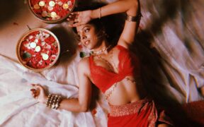 Shreya Jain wearing red lying down next to pot of rose petals