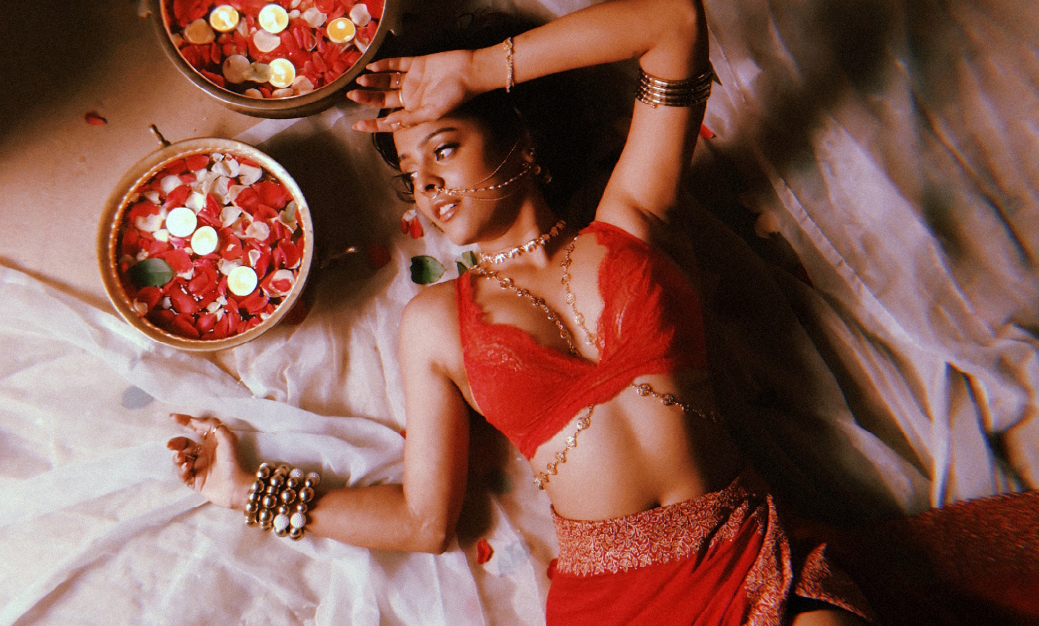 Shreya Jain wearing red lying down next to pot of rose petals