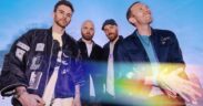 Coldplay members in jackets standing against blue sky backdrop