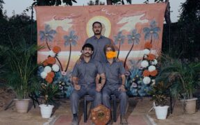 Excise Dept music group's members sitting in matching grey safari suits posing for a photo with a painted backdrop