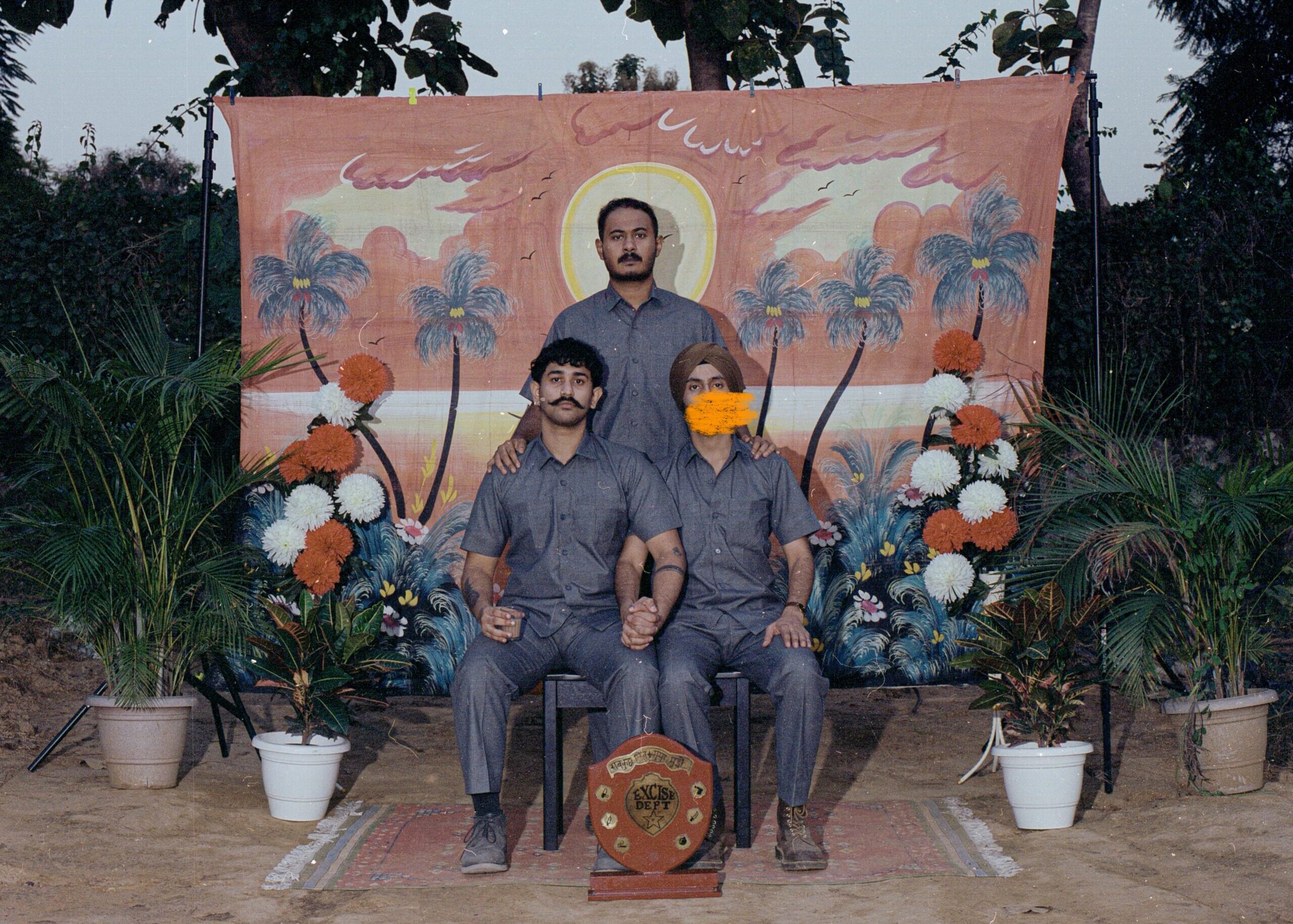 Excise Dept music group's members sitting in matching grey safari suits posing for a photo with a painted backdrop