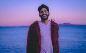 Theajsound aka Arjun Bhat wearing red coat on white tshirt and smiling