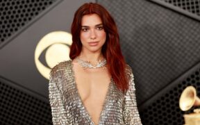 Dua Lipa with red hair, wearing a low cut gown