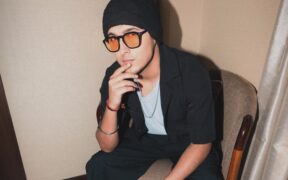 Aditya Rikhari wearing black shirt over white/grey tshirt and orange lens glasses and black cap