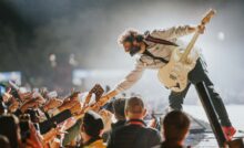 Arijit Singh holding guitar and outstretching his hand to greet fans on stage