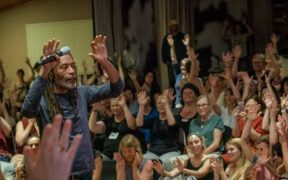 Bobby McFerrin raising his hands in a group of people at a concert workshop