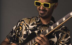 Chirag Todi in a black print shirt, wearing yellow rimmed glasses and playing guitar