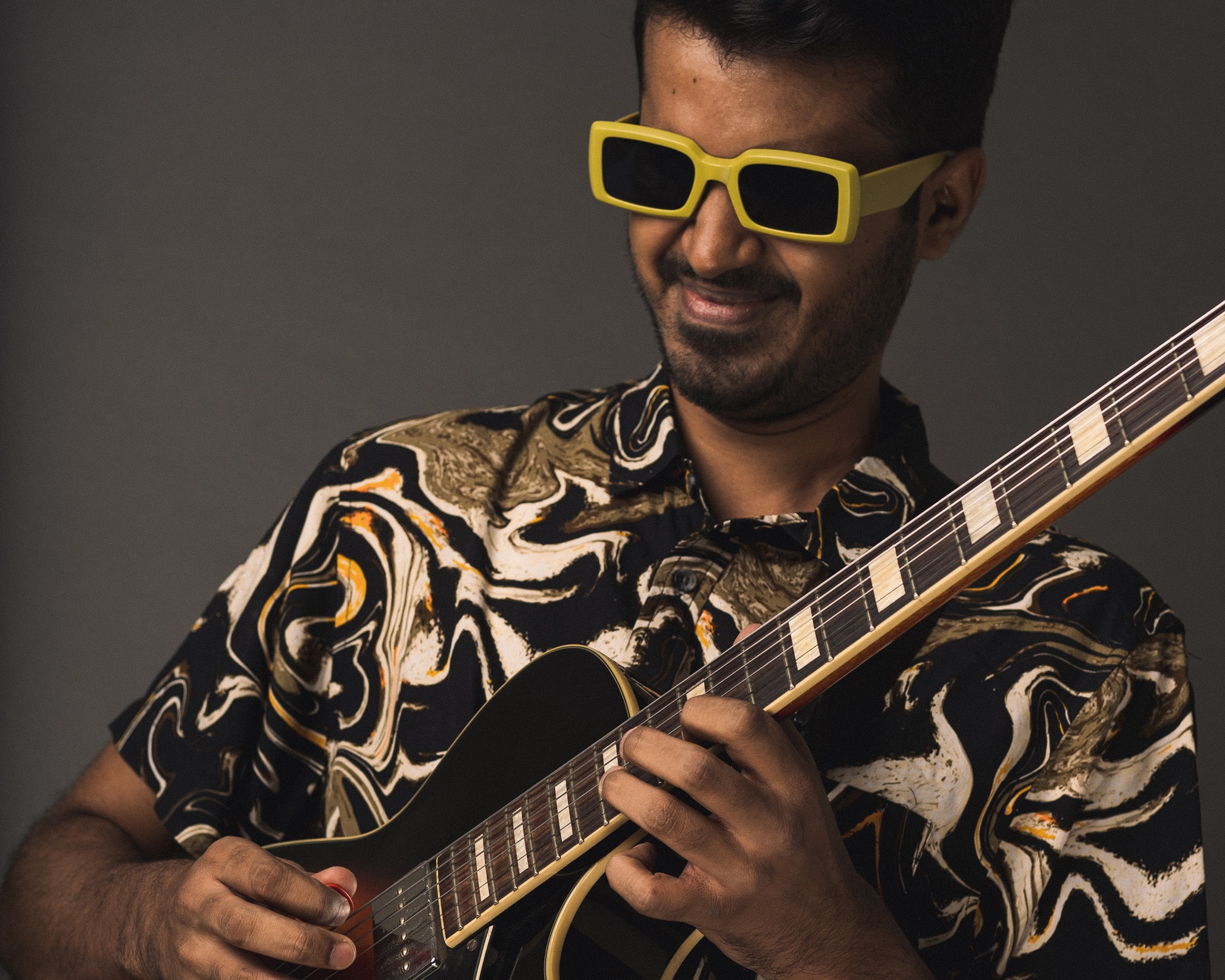 Chirag Todi in a black print shirt, wearing yellow rimmed glasses and playing guitar