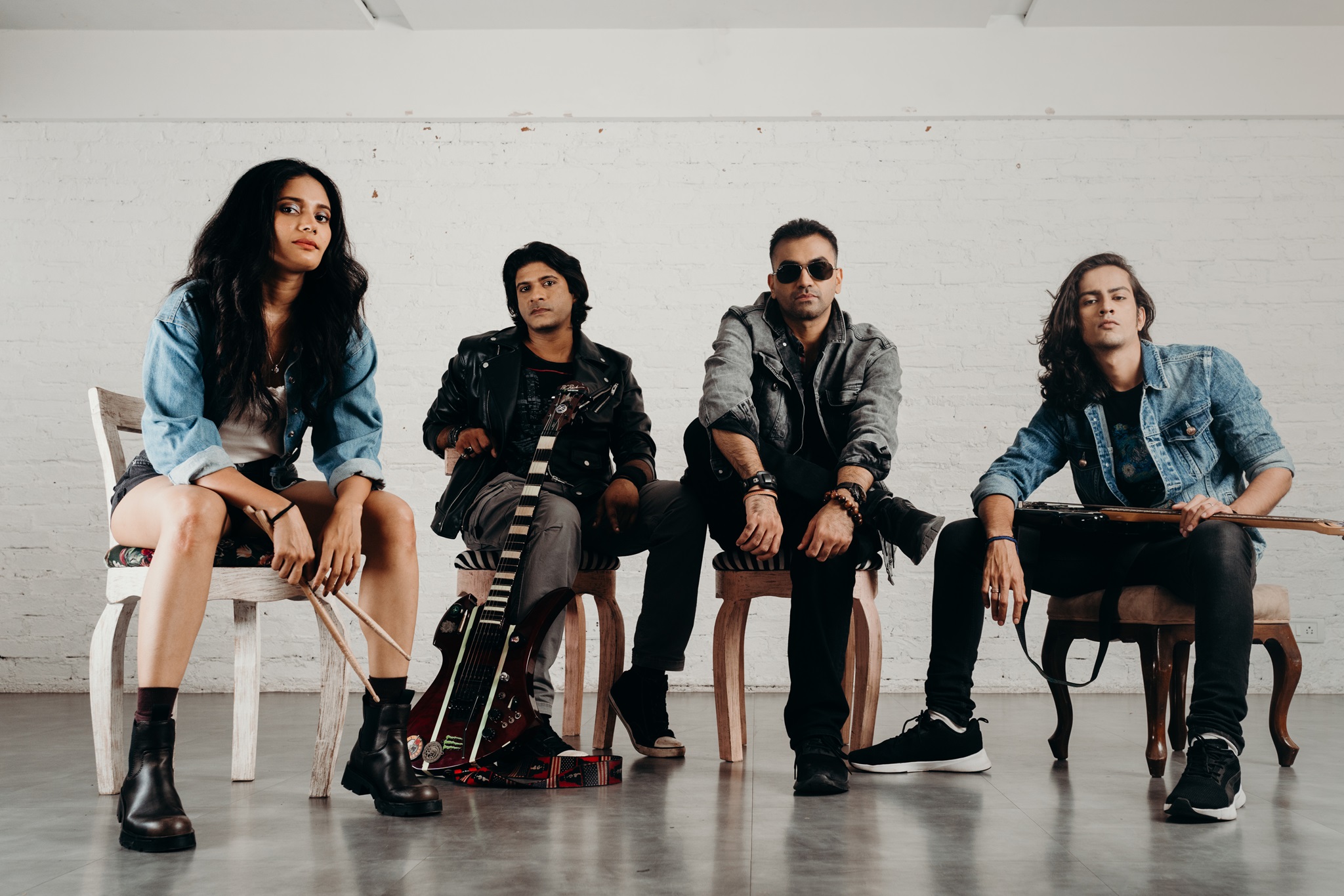 Members of Mumbai rock band Contra seated and posing for a photo with their instrumentsi ncluding bass guitar and electric guitar and drumsticks