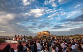 Crowd gathered to watch a performance of artists under blue sky at Mehrangarh Fort