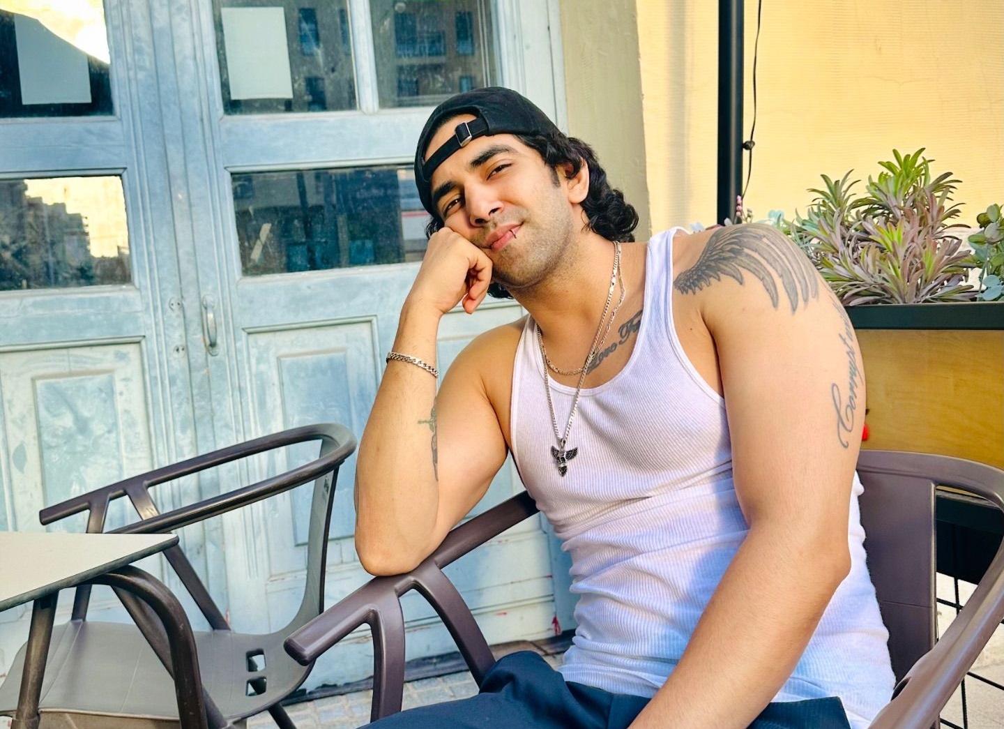 Vilen artist wearing white vest and cap, sitting on chair with hand to his face