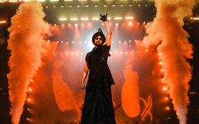 Diljit Dosanjh performing on stage wearing all black with smoke in the background