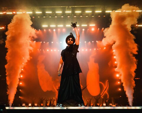 Diljit Dosanjh performing on stage wearing all black with smoke in the background