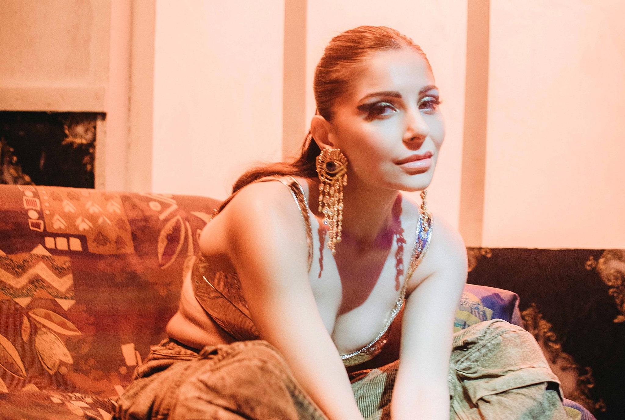 Kanika Kapoor seated on a couch with her arms in front of her, smiling with big earrings