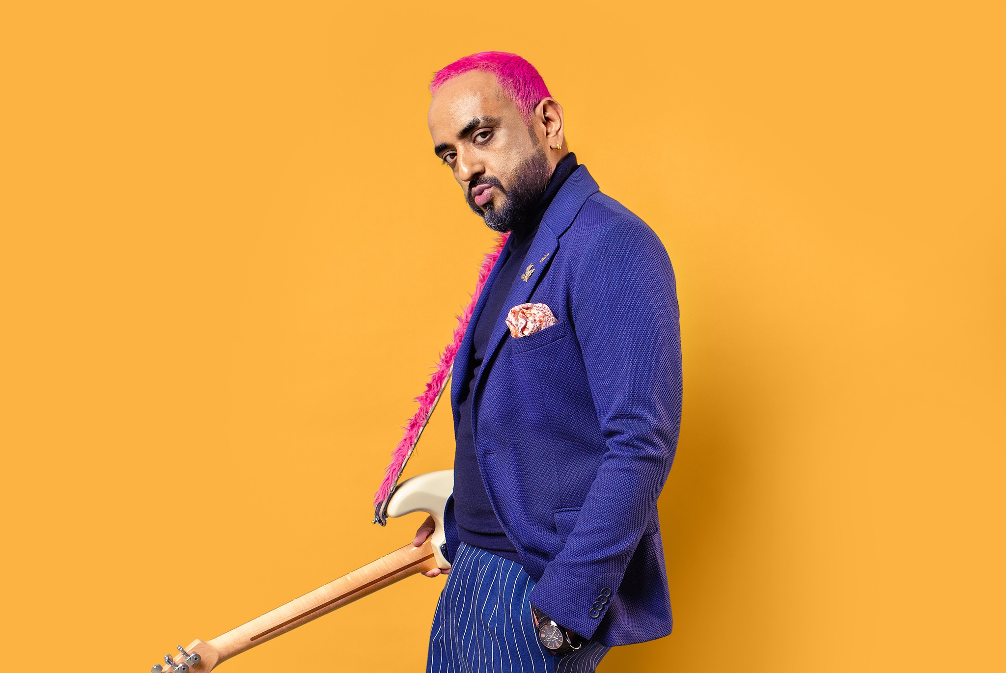 Sanjeev T aka Kulture Cid wearing blue coat and pants, pink hair and holding white guitar