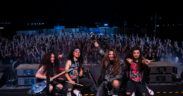 Band members of Girish and the Chronicles pose for a photo on stage with the audience in the background at a concert