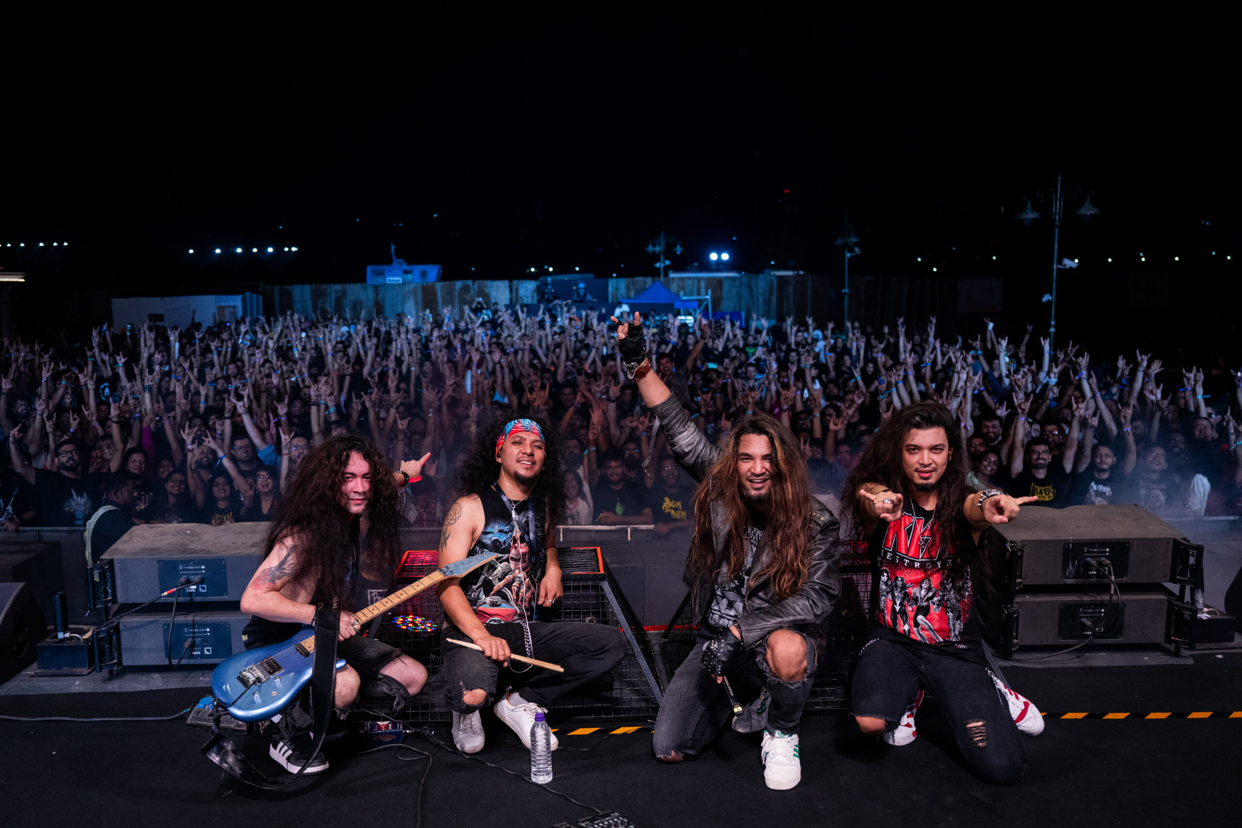 Band members of Girish and the Chronicles pose for a photo on stage with the audience in the background at a concert