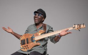 Richard Bona with hands in the air sitting down with a bass guitar