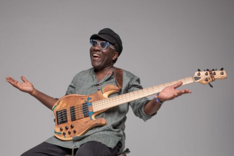 Richard Bona with hands in the air sitting down with a bass guitar