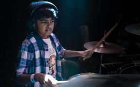 Sanidhya Das wearing plaid shirt and white tshirt playing drums