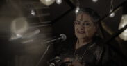 Usha Uthup in a black saree, holding a tambourine.