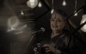 Usha Uthup in a black saree, holding a tambourine.