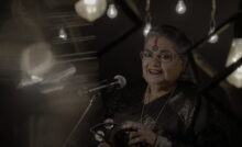 Usha Uthup in a black saree, holding a tambourine.