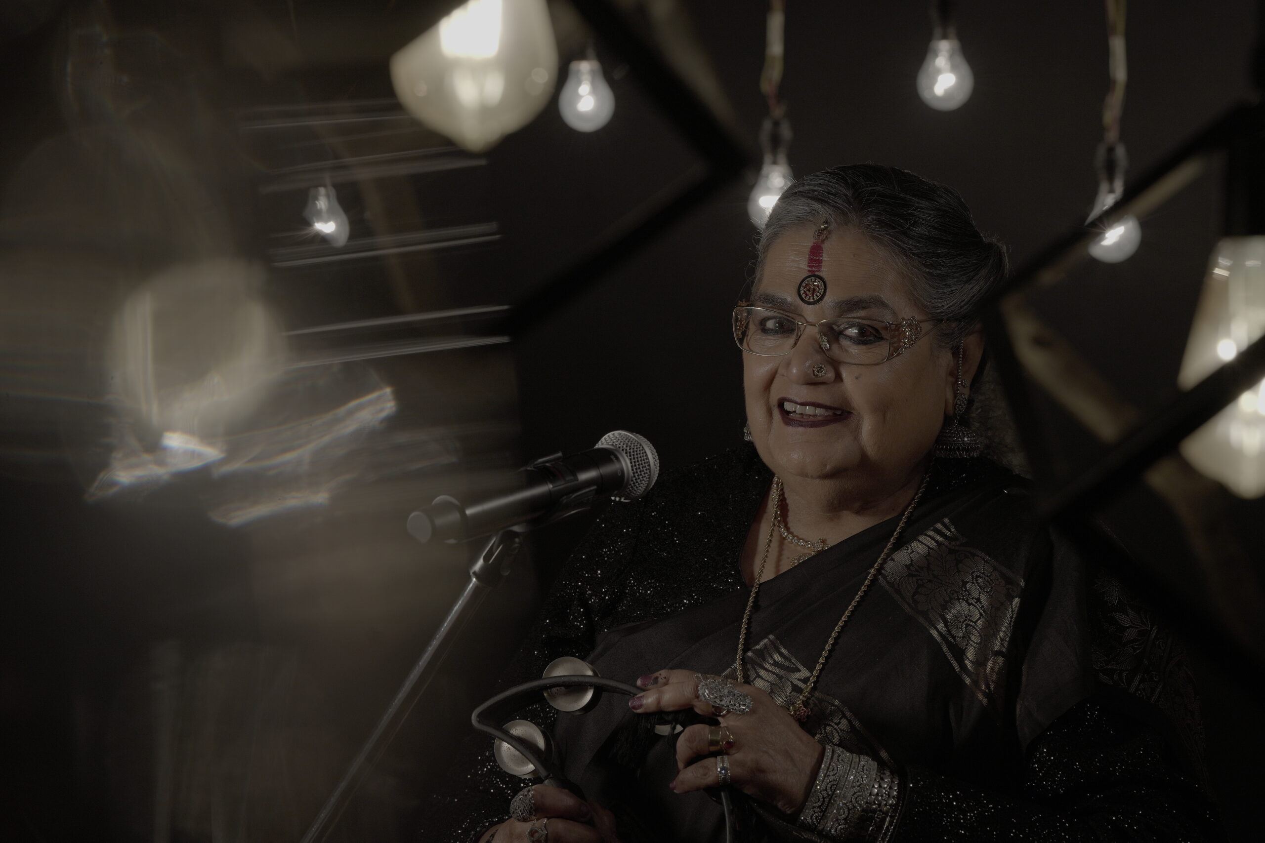 Usha Uthup in a black saree, holding a tambourine.