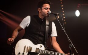 Alluri playing guitar wearing black vest and white shirt