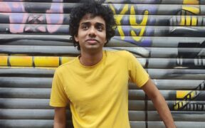 Music composer Topshe aka Dhritiman Das in a yellow tshirt posing in front of a shutter with graffiti