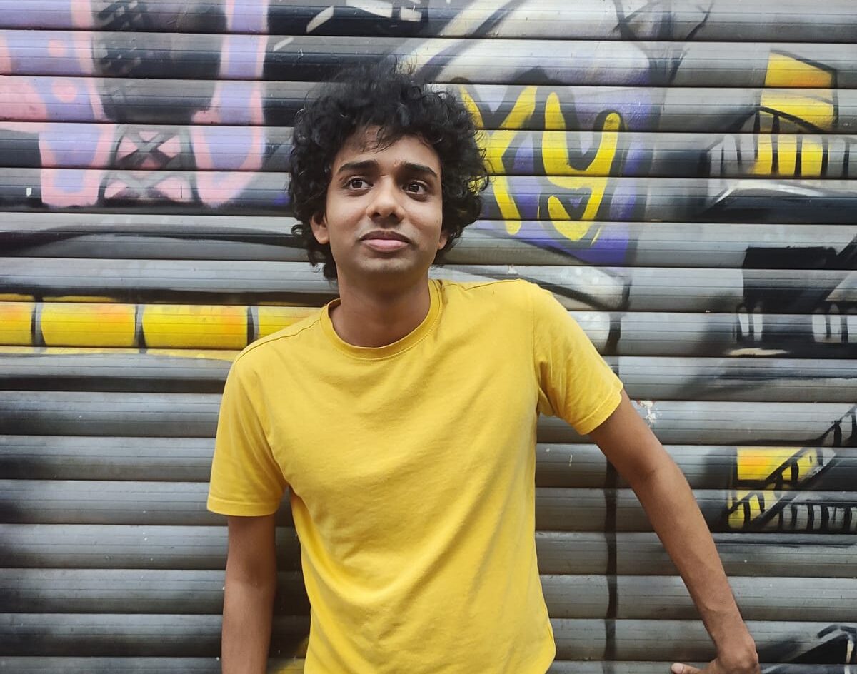 Music composer Topshe aka Dhritiman Das in a yellow tshirt posing in front of a shutter with graffiti