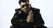 Yashraj wearing black jacket and pants, and sunglasses with hands folded