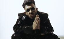 Yashraj wearing black jacket and pants, and sunglasses with hands folded