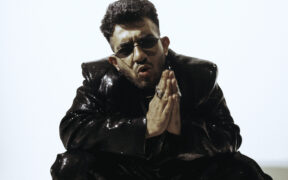 Yashraj wearing black jacket and pants, and sunglasses with hands folded