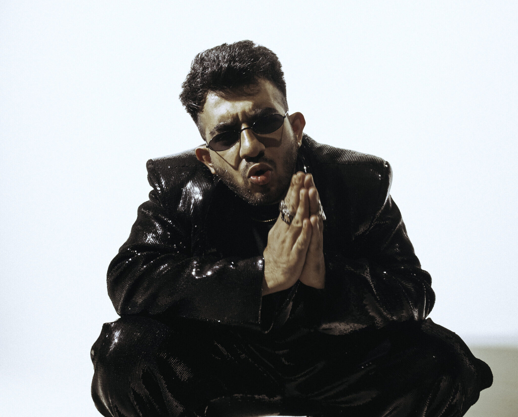 Yashraj wearing black jacket and pants, and sunglasses with hands folded